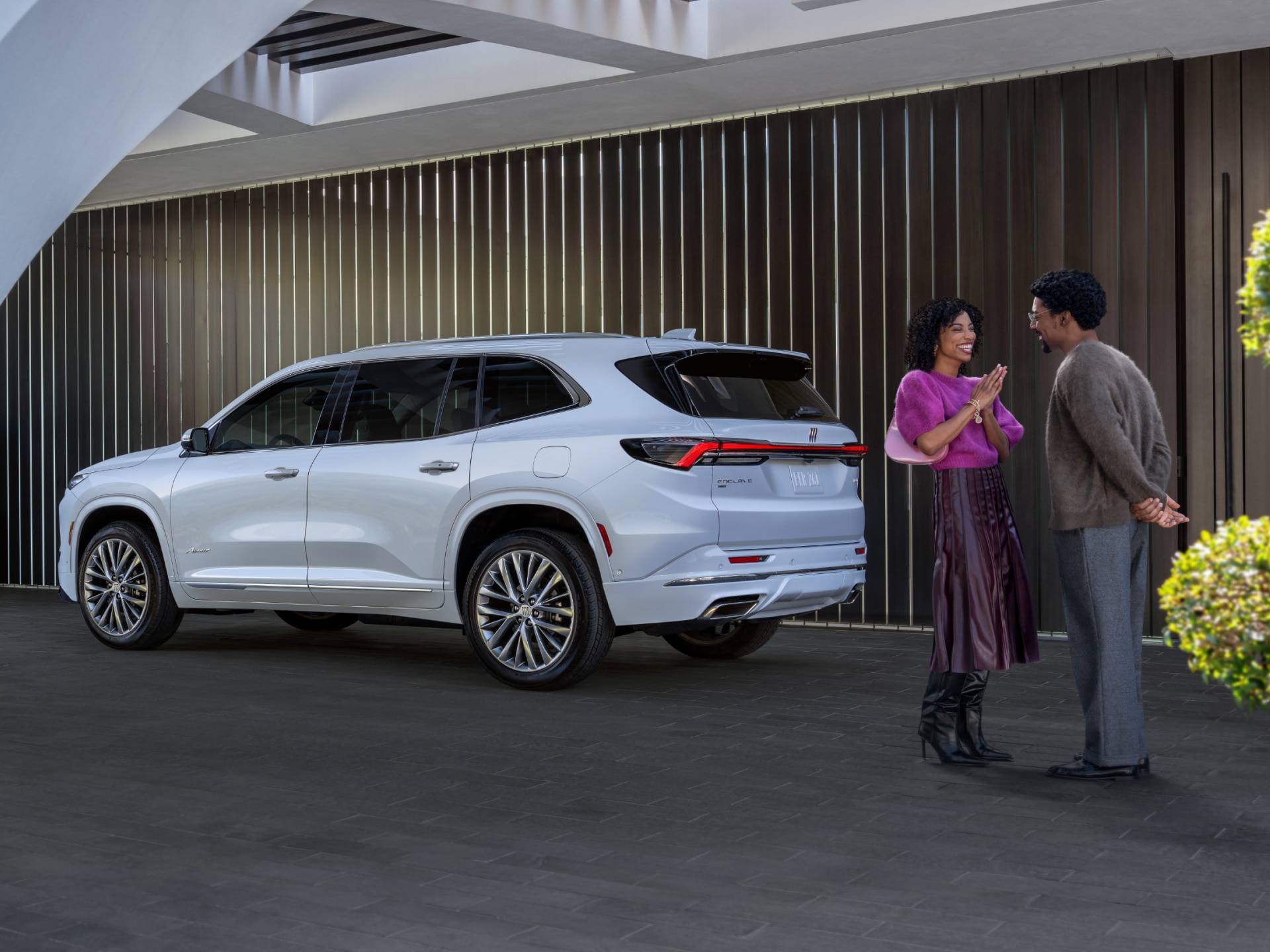 A Man And Woman Holding Hands Walking Towards a White Buick Enclave SUV Parked Outside a Modern Building