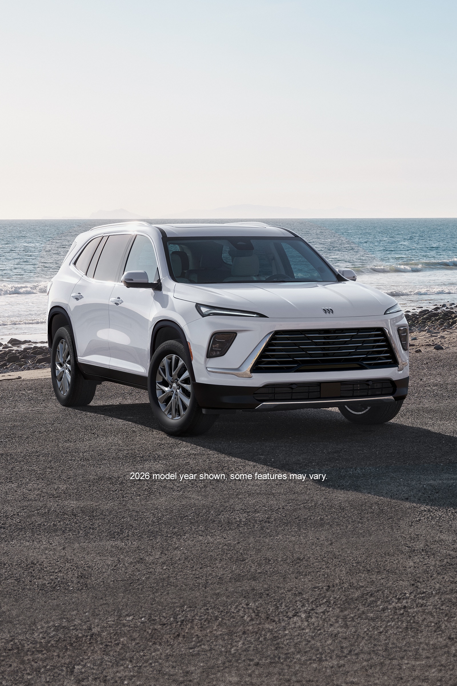 A White Buick Enclave SUV Parked on an Asphalt Road With the Ocean and Beach in the Background