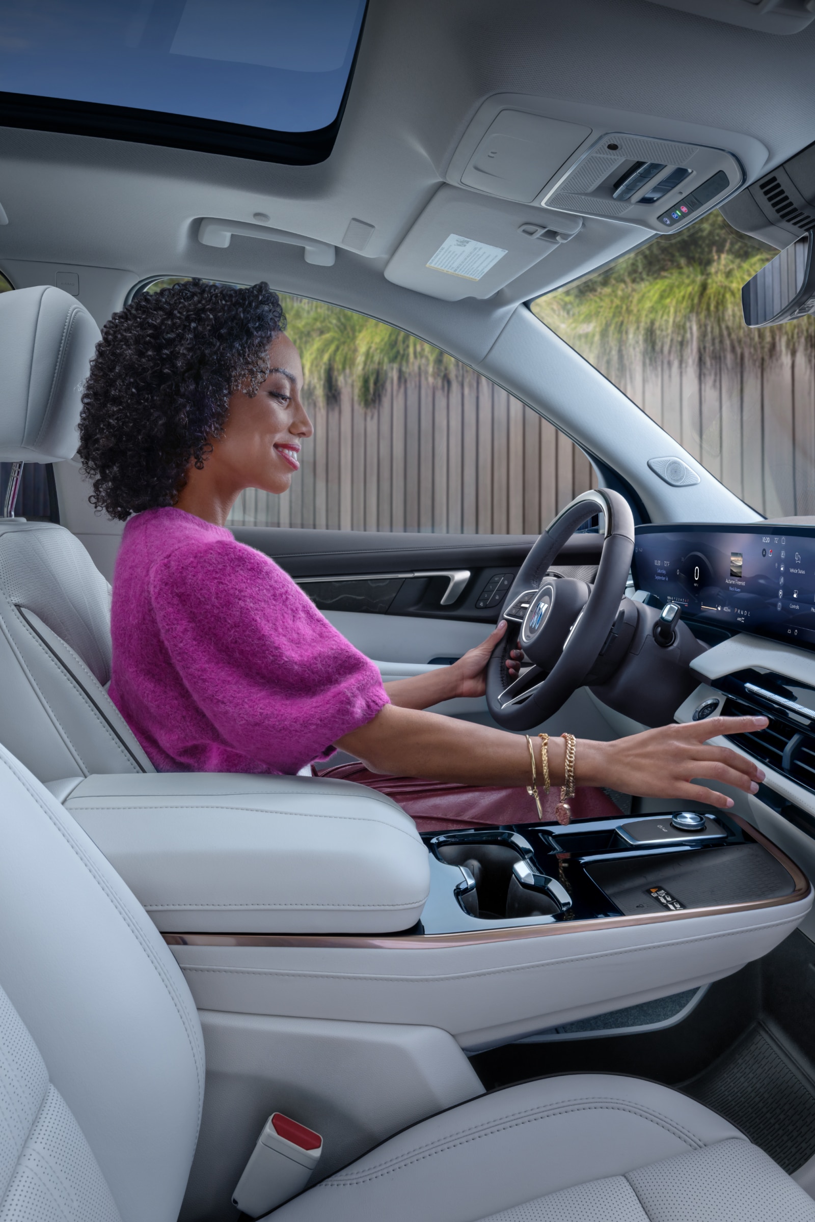 A Woman in a Pink Sweater Driving a Buick Vehicle with a Light-Colored Interior and a Large Infotainment Screen