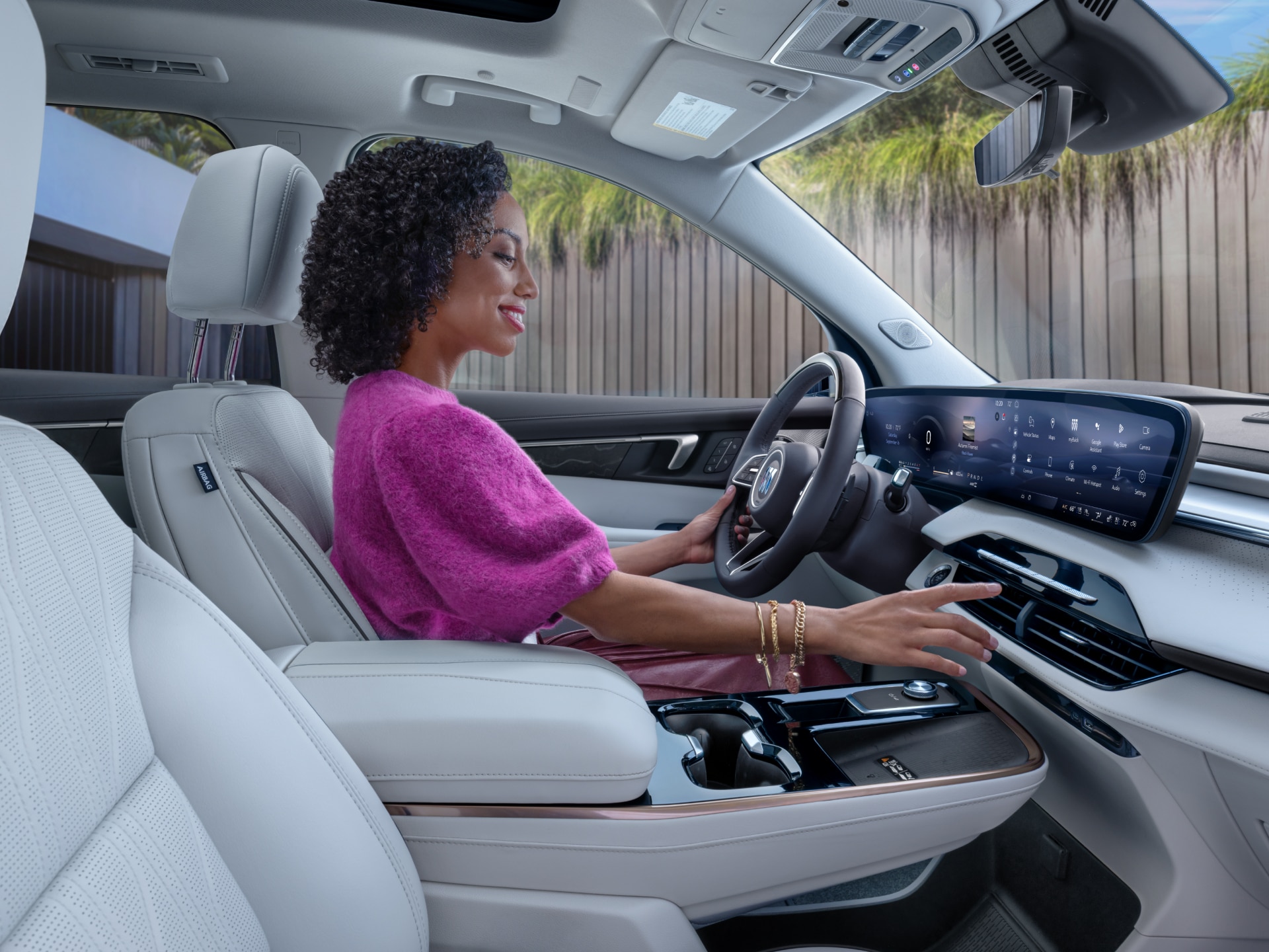 A Woman in a Pink Sweater Driving a Buick Vehicle with a Light-Colored Interior and a Large Infotainment Screen