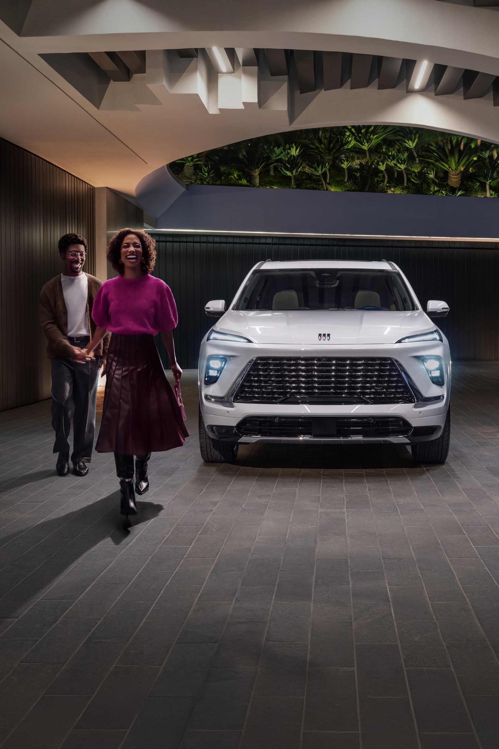 A Man and a Woman Walking Away From a White Buick Enclave SUV Parked in a Modern Garage