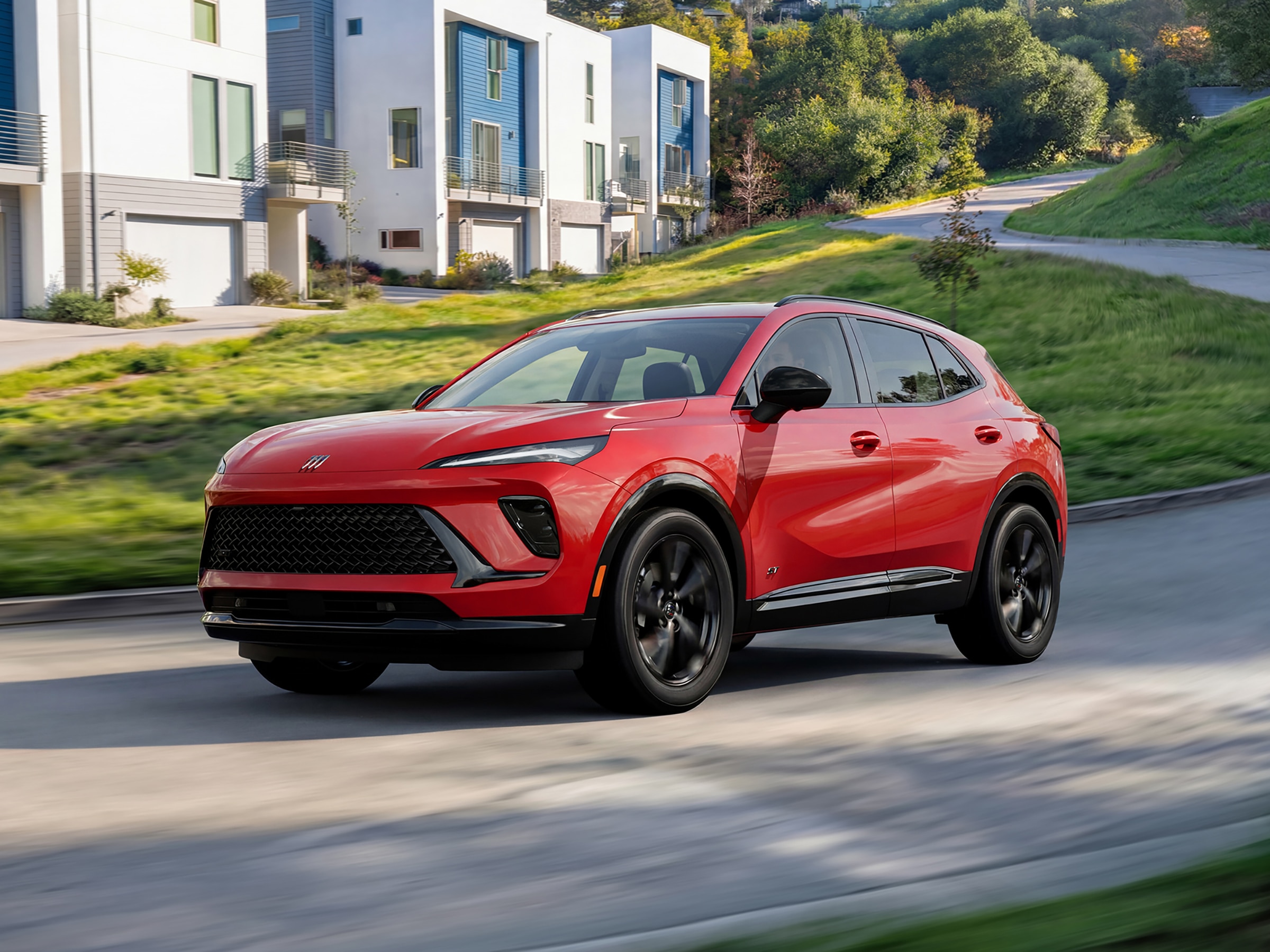 Profile View of the 2026 Buick Envision in Brilliant Red Driving Downhill on a Curvy Road