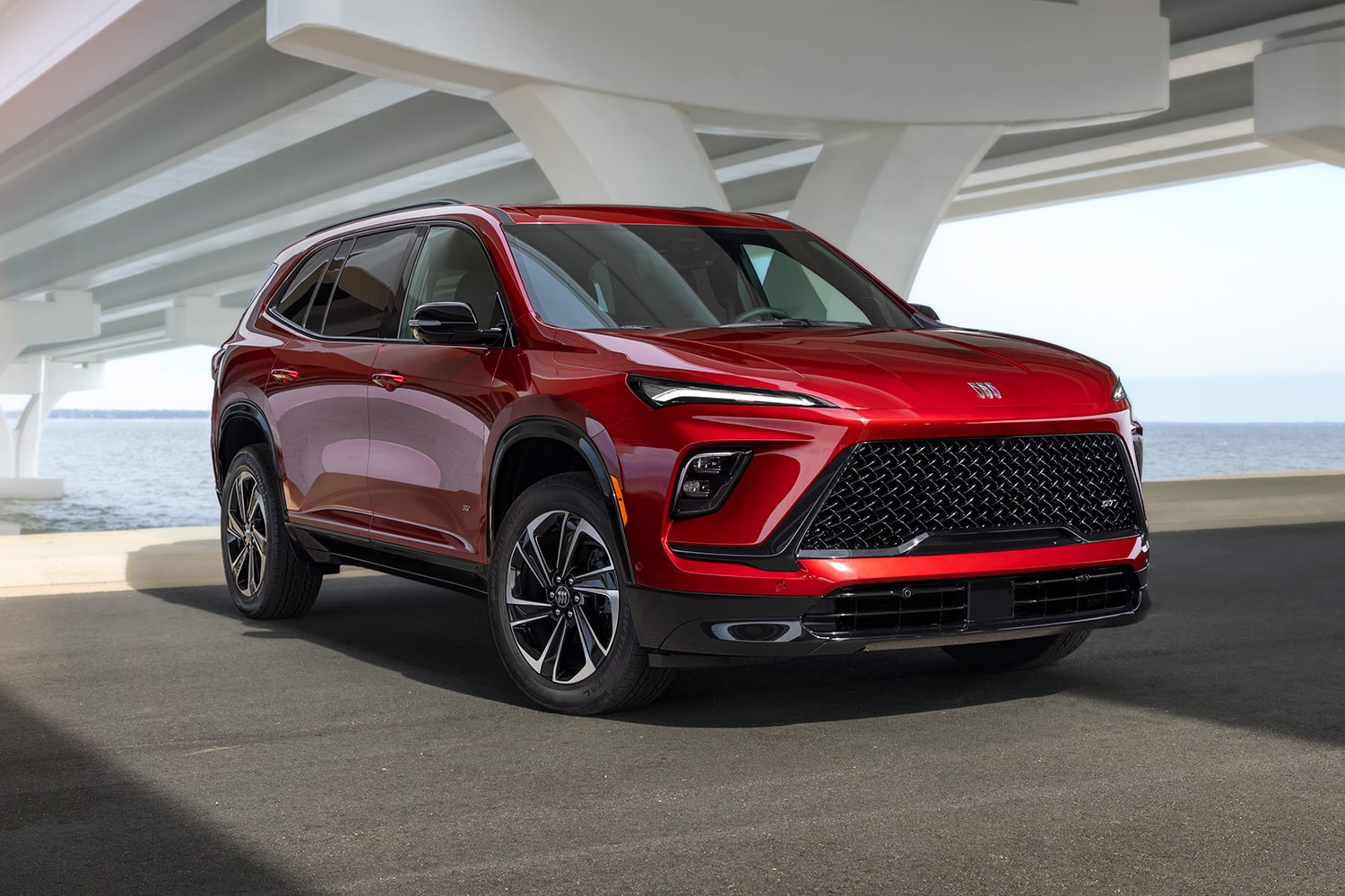 A Red Buick SUV Parked by the Water under a Concrete Bridge Structure