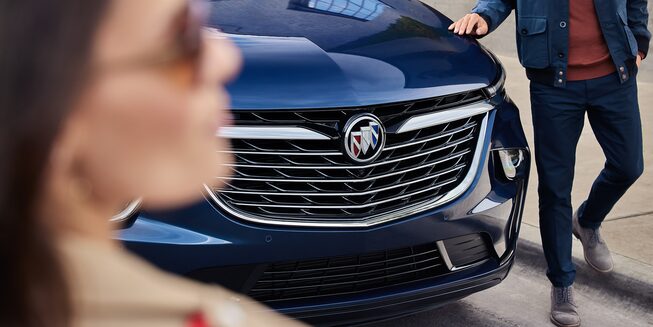 A Woman Looking Away as a Man Stands By the Buick Enclave