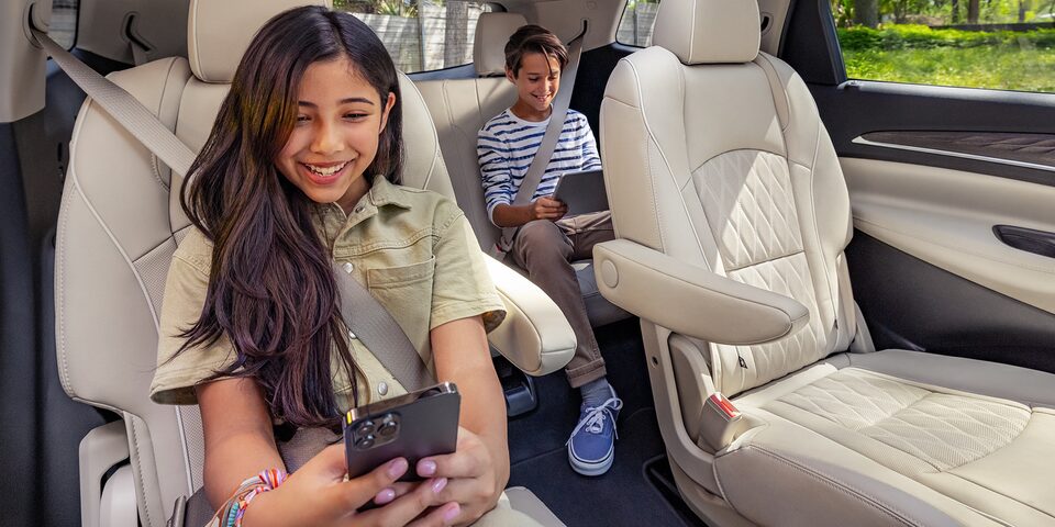 A Young Girl and Her Little Brother Enjoy Their Cell Pone & Tablets While Sitting Comfortably in Their Buick Enclave