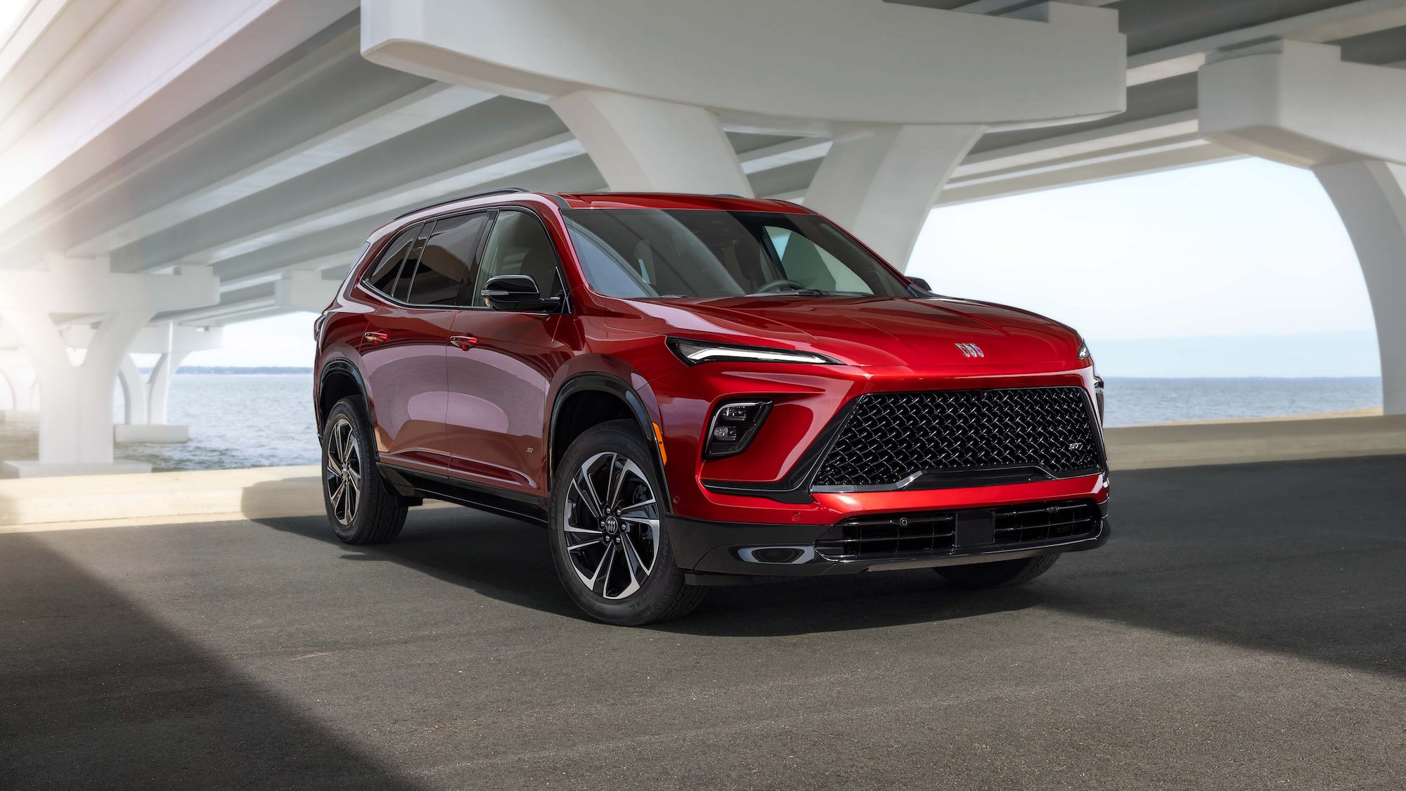 Three-Quarters View of a 2026 Red Buick Enclave Mid-Size SUV Parked Under a Bridge