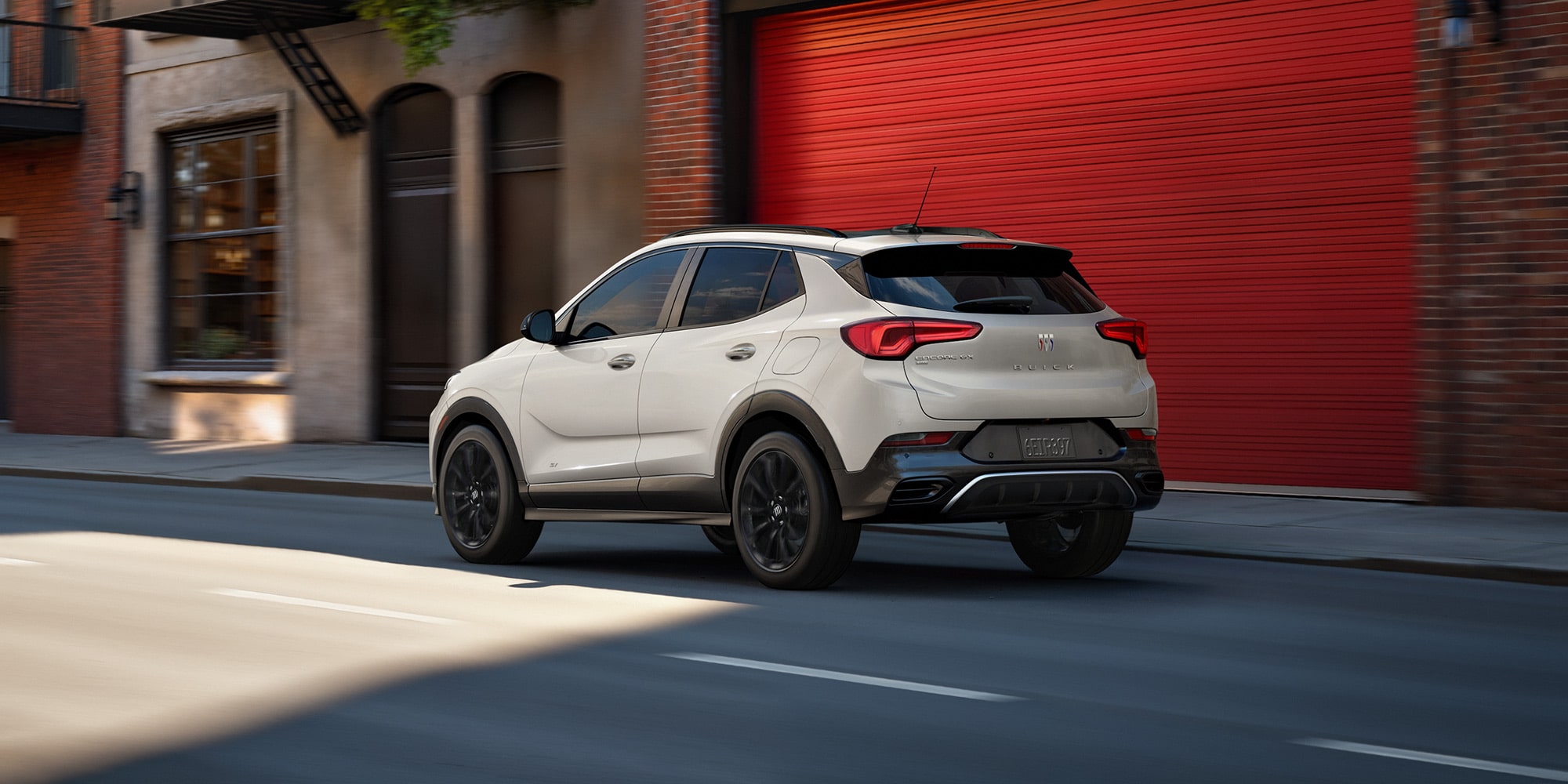 The 2026 Buick Encore GX Sports Touring SUV in the Color Ceramic Driving Down a City Street