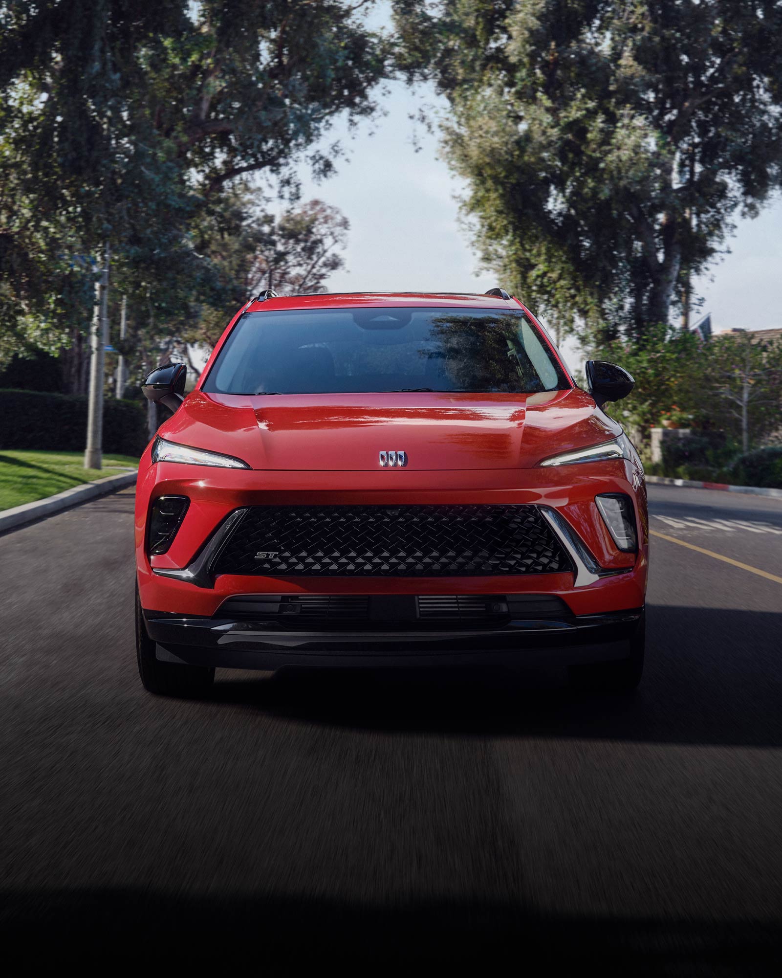 Front View of the 2026 Buick Envision ST Sporty Compact SUV Driving Down a Black Top Road