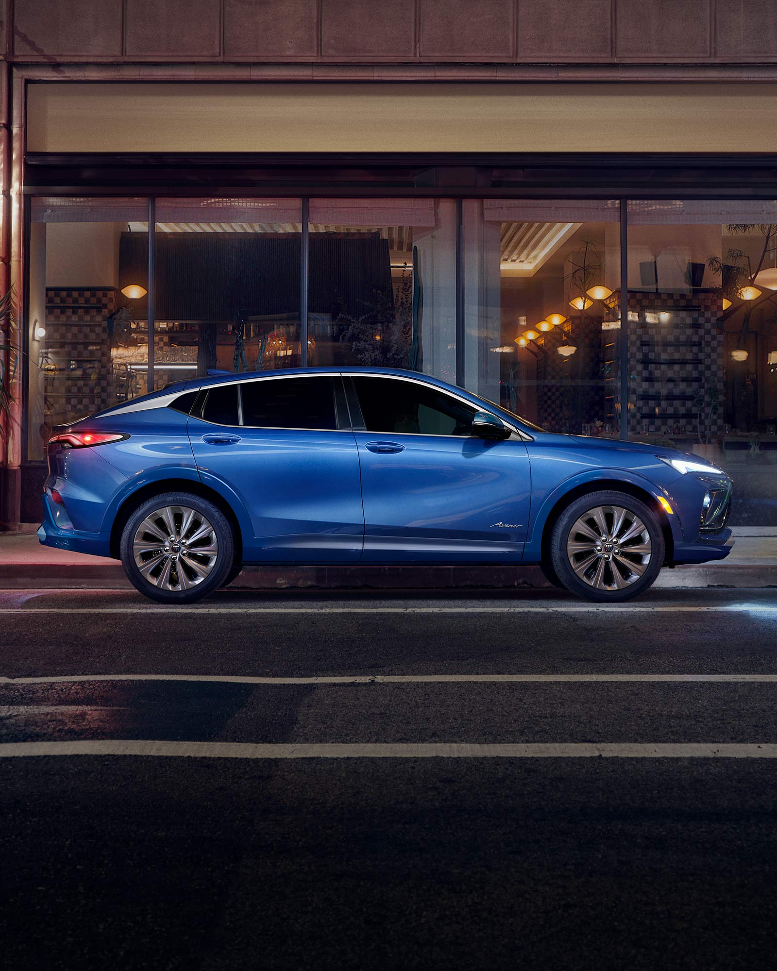 Side View of a Blue 2026 Buick Envista Sport Touring Sport SUV Driving Through Downtown at Night
