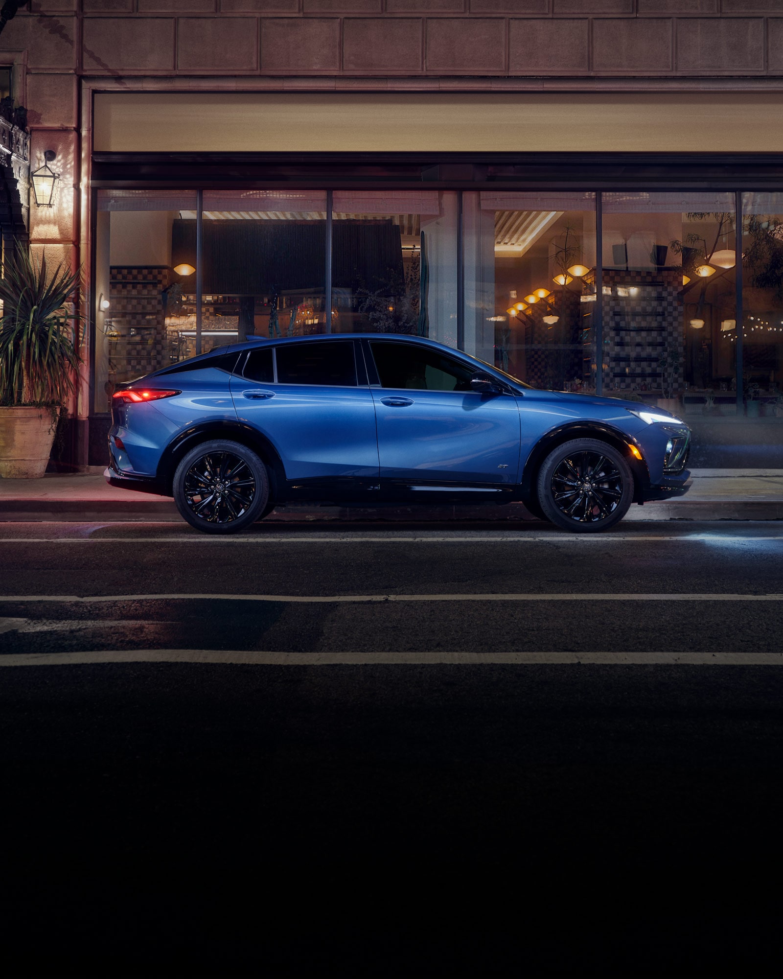 Side View of a Blue 2026 Buick Envista Sport Touring Sport SUV Driving Through Downtown at Night