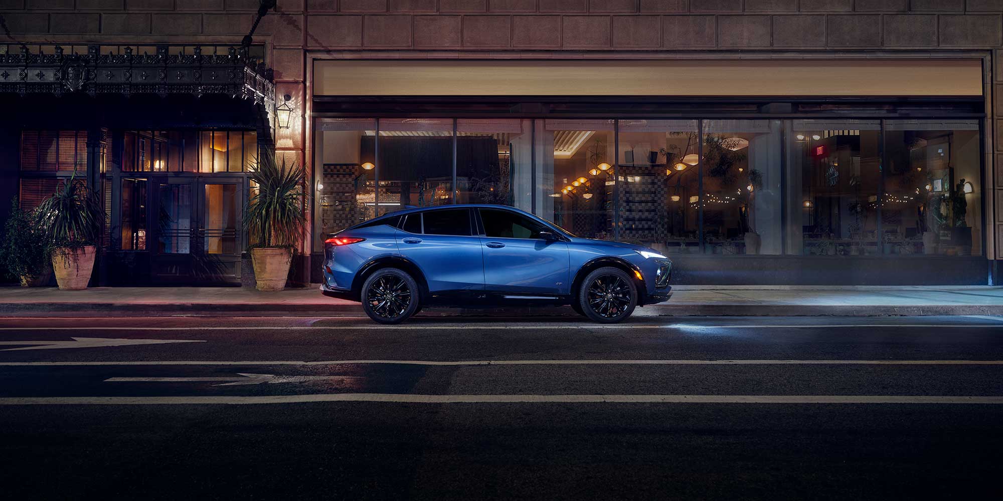 Side View of a Blue 2026 Buick Envista Sport Touring Sport SUV Driving Through Downtown at Night