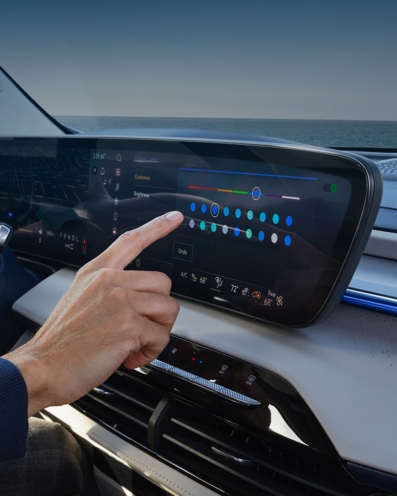 A Hand Interacting with a Car's Infotainment Touchscreen to Adjust Ambient Lighting Settings with the Ocean in the Background