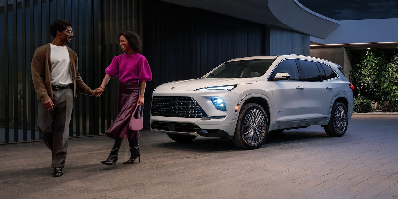 A Couple Holding Hands and Walking Away From a White Buick Enclave SUV Parked Outside