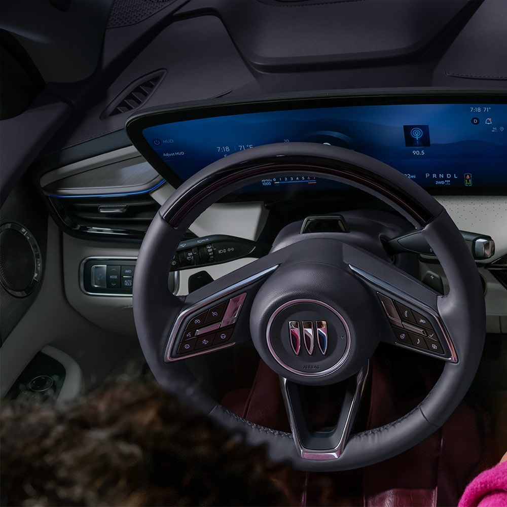 A Driver's Hand Interacts with the Expansive Curved Digital Display in a Modern Buick Interior, Featuring the Buick Logo on the Steering Wheel