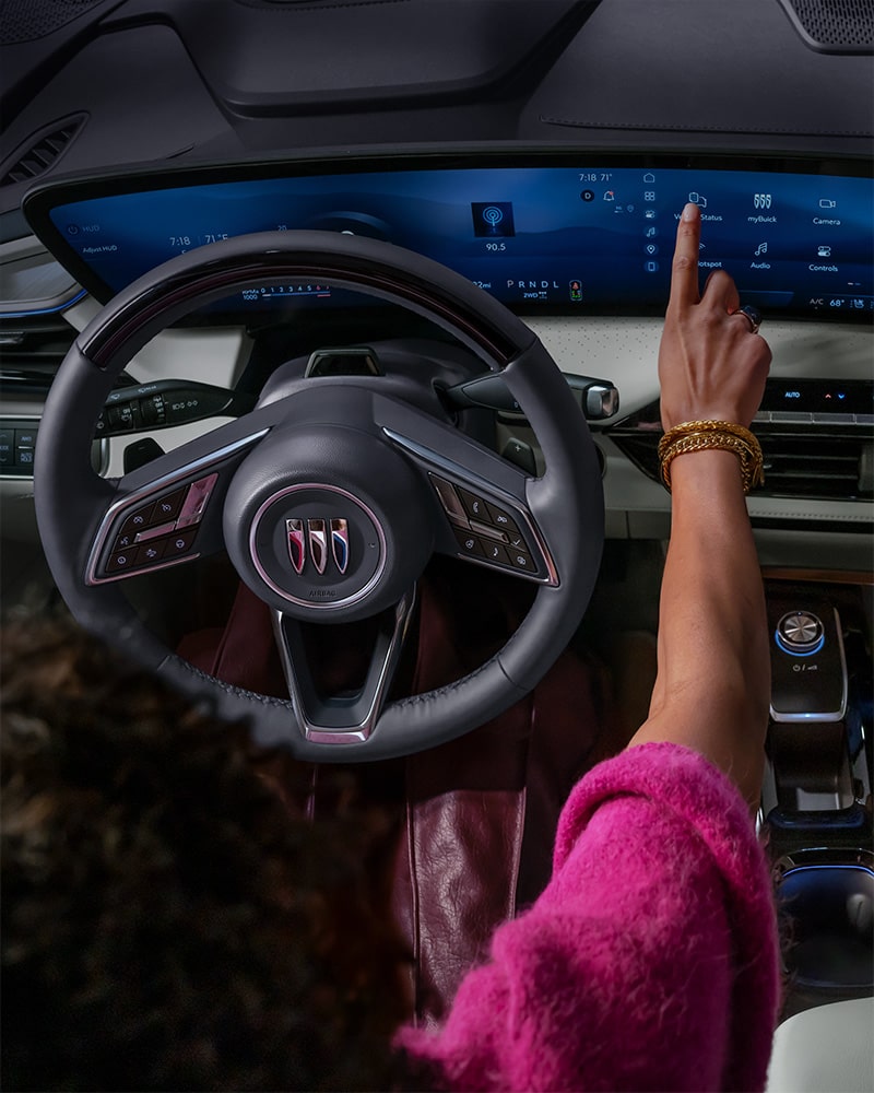 A Driver's Hand Interacts with the Expansive Curved Digital Display in a Modern Buick Interior, Featuring the Buick Logo on the Steering Wheel