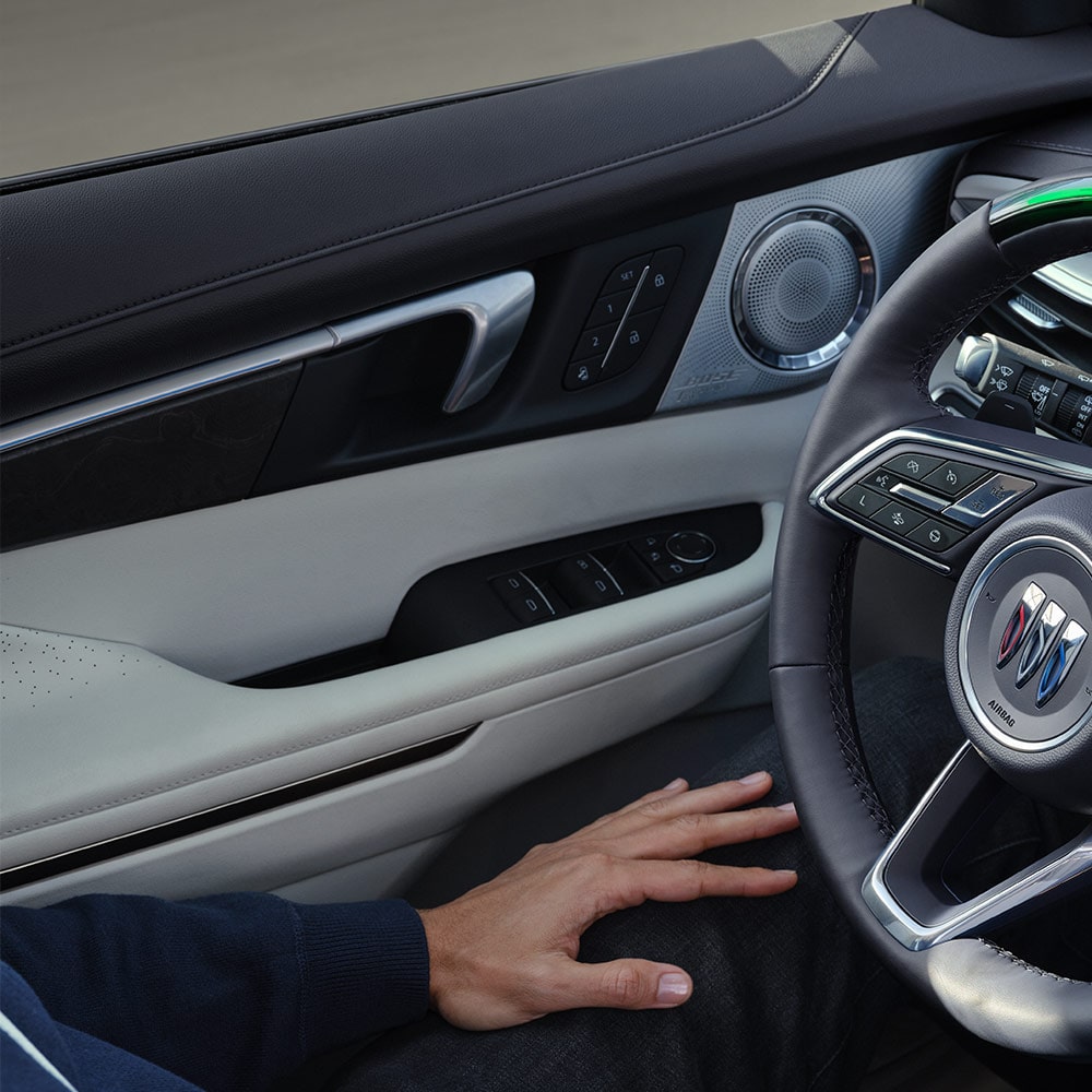 A Driver's Hand Resting on their Lap with a View of the Buick Steering Wheel and Car Door Panel