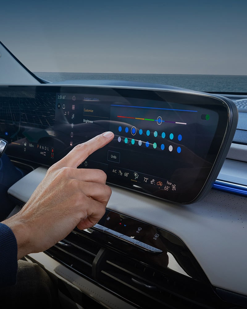 A Hand Interacting with a Car's Infotainment Touchscreen to Adjust Ambient Lighting Settings with the Ocean in the Background