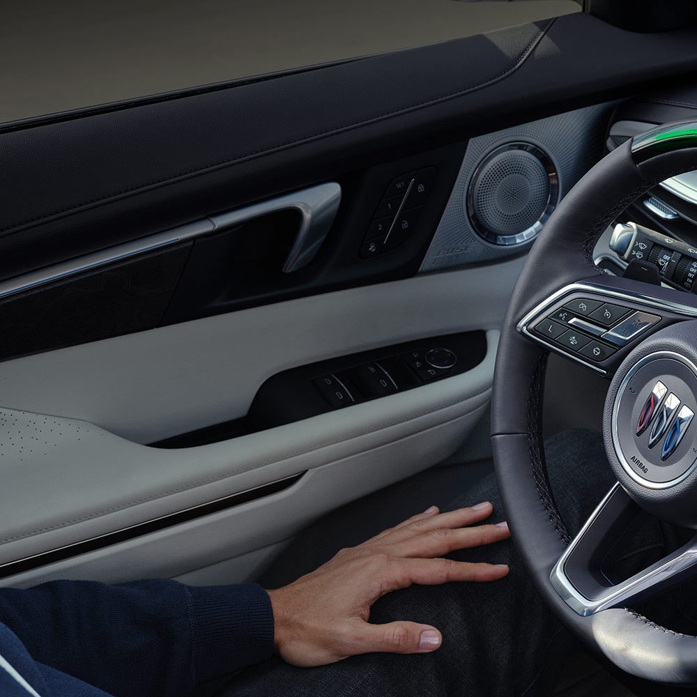 A Driver's Hand Resting on their Lap with a View of the Buick Steering Wheel and Car Door Panel