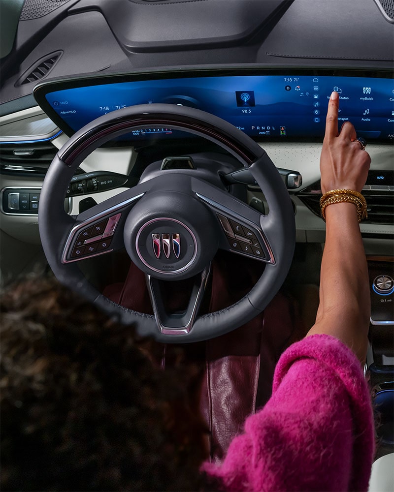 A Driver's Hand Interacts with the Expansive Curved Digital Display in a Modern Buick Interior, Featuring the Buick Logo on the Steering Wheel