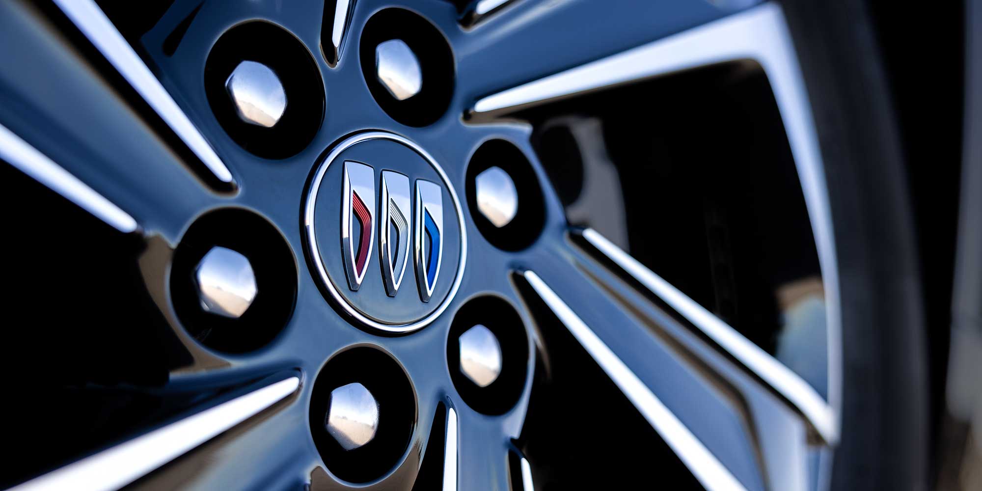 A Close-up View of a Glossy Black Car Wheel with Silver Spokes and the Buick Logo in the Center