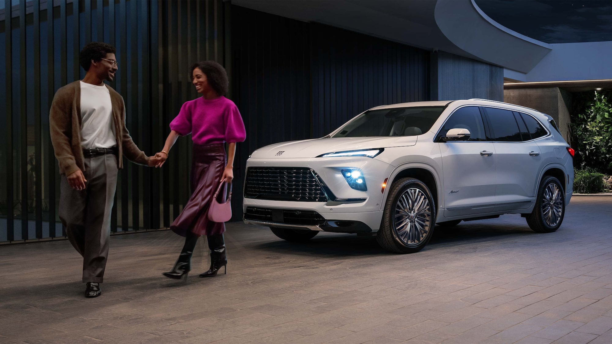 A Couple Holding Hands and Walking Away From a White Buick Enclave SUV Parked Outside