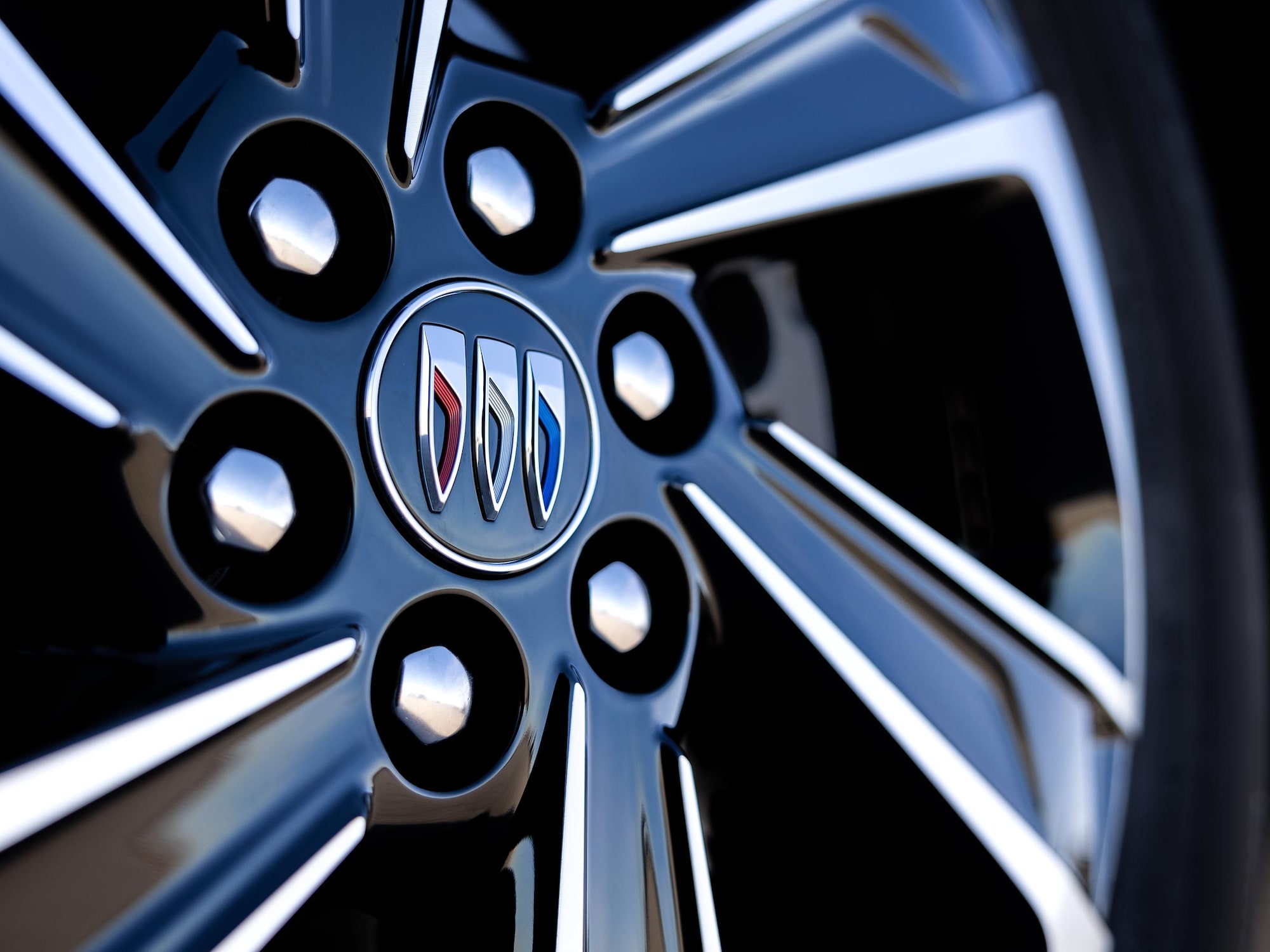 A Close-up View of a Glossy Black Car Wheel with Silver Spokes and the Buick Logo in the Center