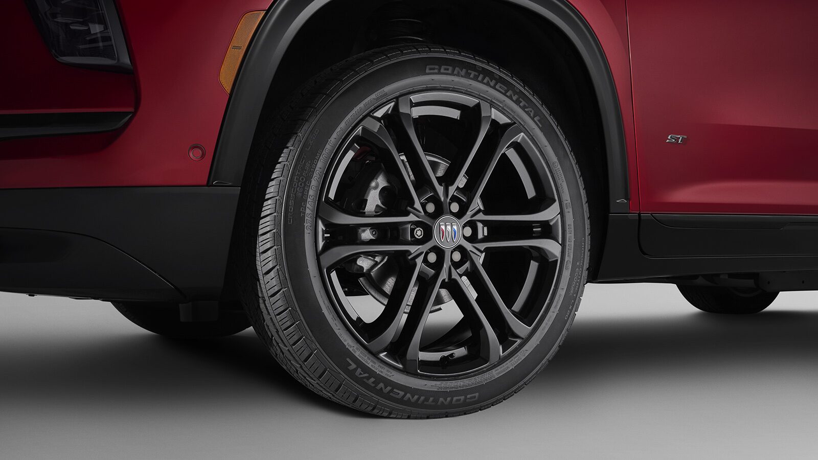 A Close-up of a Black Multi Spoke Wheel with a Buick Logo on a Red Buick SUV
